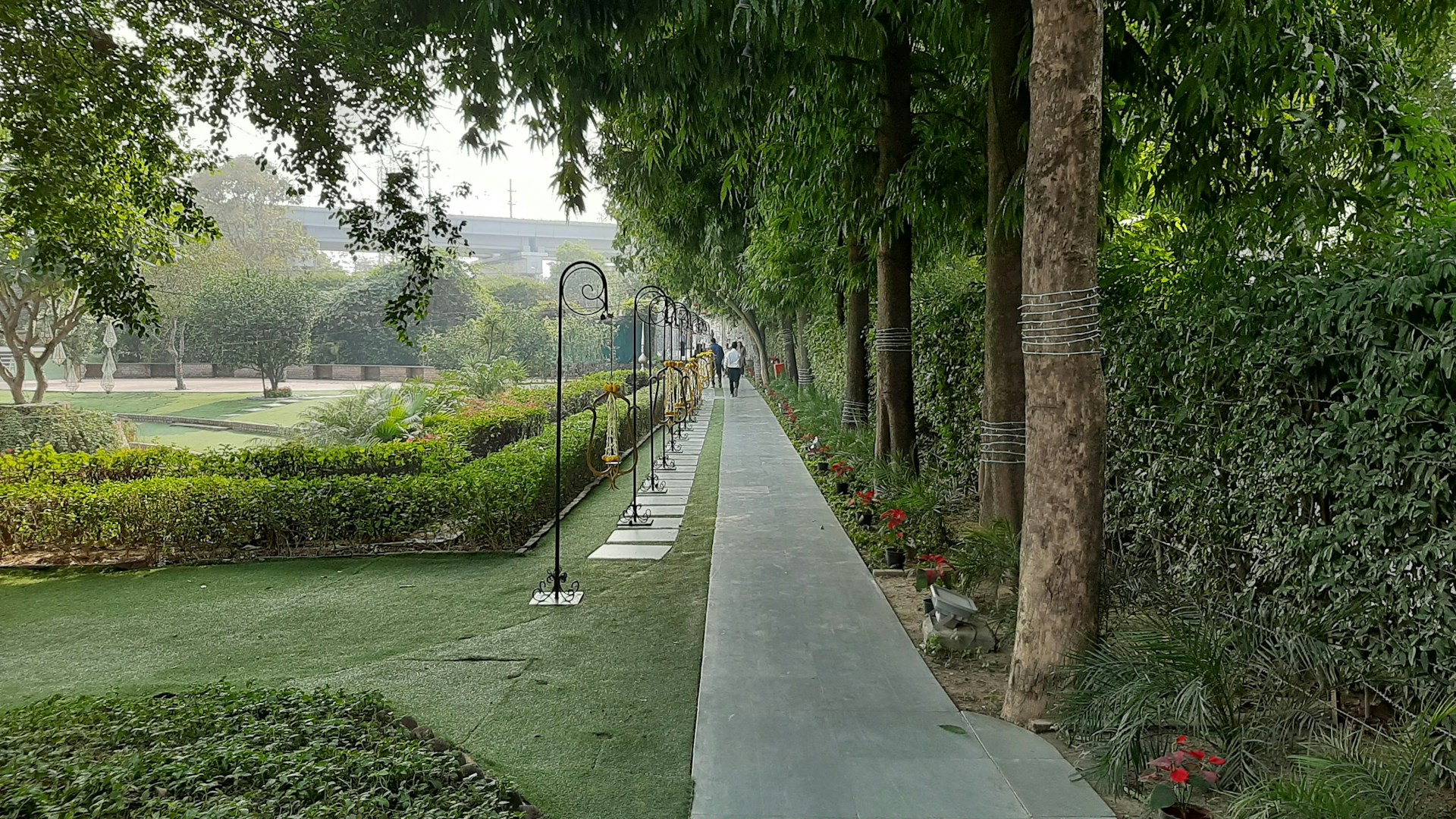A peaceful pathway lined with neatly trimmed greenery and elegant Islamic architectural elements at Al Azhar Memorial Garden in Karawang Timur.