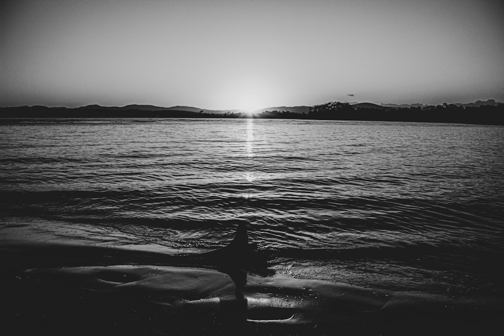 Graustufenfoto einer Person, die auf einem Felsen im Meer sitzt