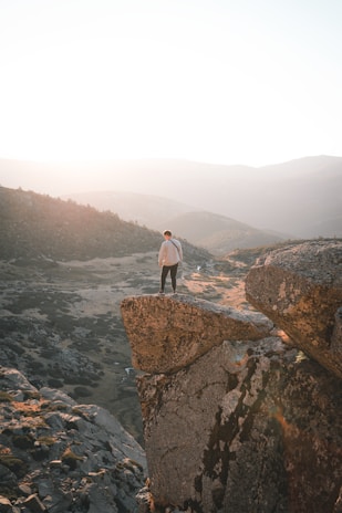 The creator of abjaustral standing on a rocky outcrop overlooking a vast valley at dawn.