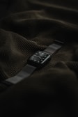 A smart watch with a dark screen and metallic strap is placed on top of a textured dark green fabric.