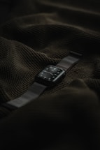 A smart watch with a dark screen and metallic strap is placed on top of a textured dark green fabric.