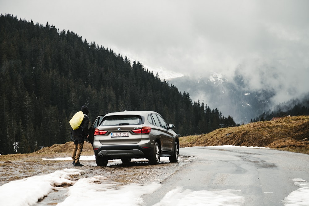 man in yellow jacket standing beside black suv on snow covered road during daytime