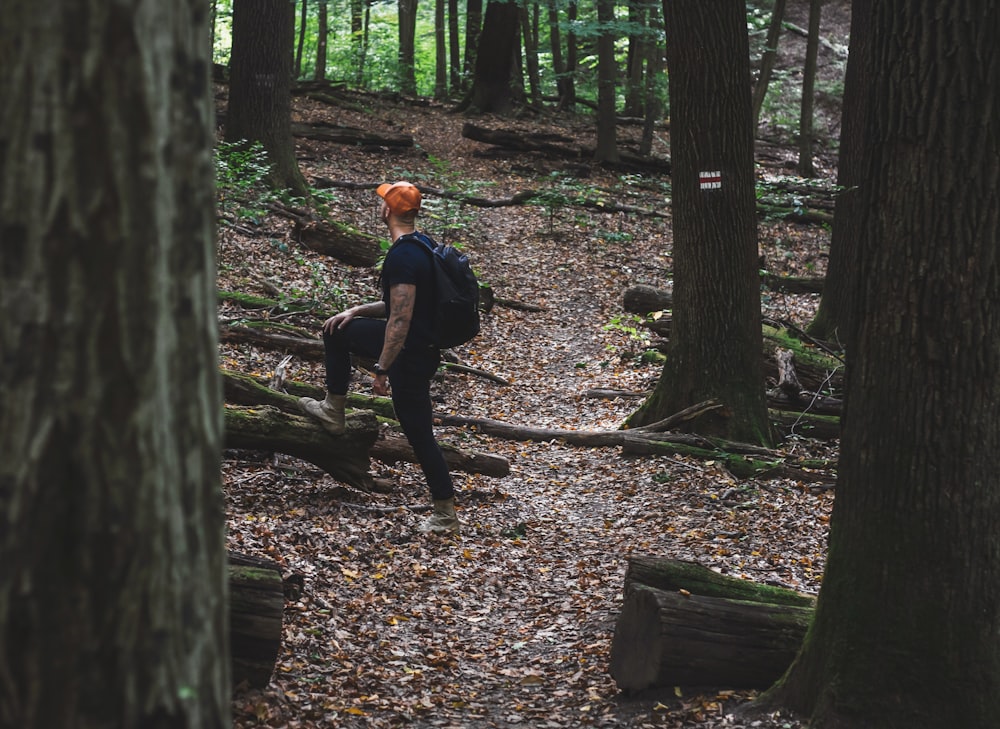 man in black t-shirt and black pants sitting on tree log during daytime