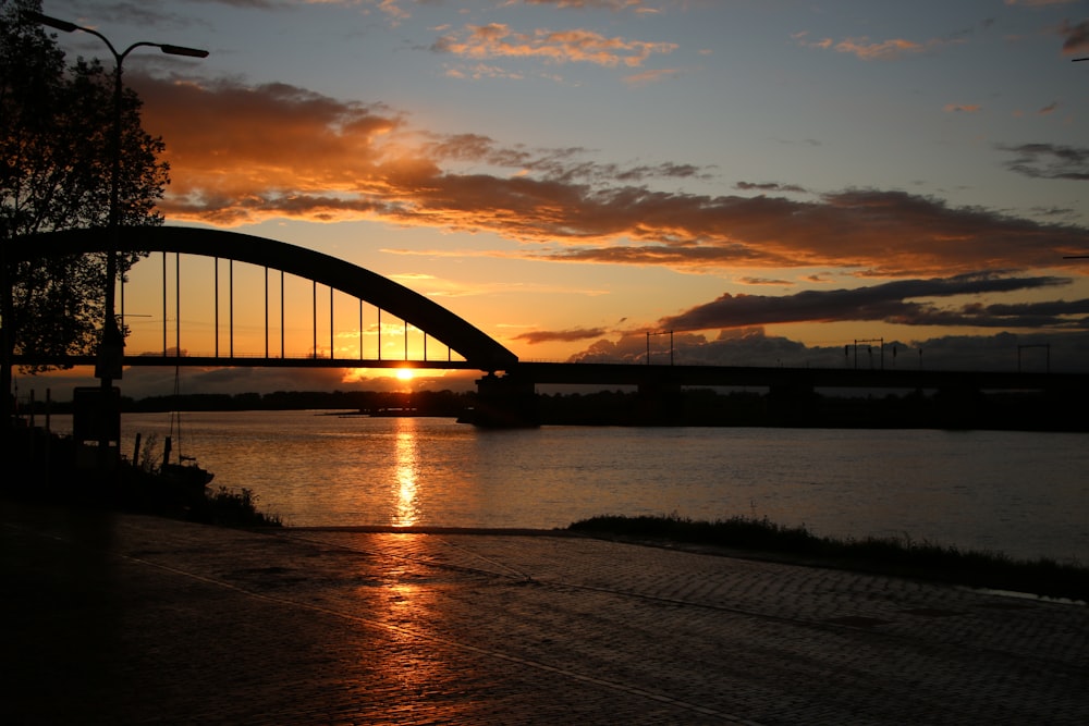 silhouette of bridge over body of water during sunset