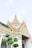An ornate temple structure featuring intricate golden spires and detailed architectural elements. The building is adorned with colorful mosaics and traditional artistic decorations, characteristic of Southeast Asian religious structures. In the foreground, there are lush green trees, enhancing the serene atmosphere.