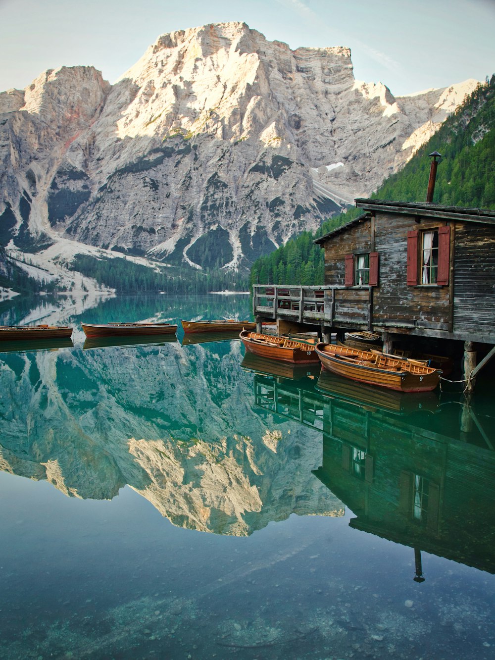 Braunes Holzhaus am grünen See in der Nähe eines schneebedeckten Berges tagsüber