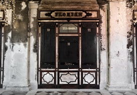 An ornate and historic looking storefront with dark wood panels and an overhead sign reading 'Florian'. The structure is flanked by two columns and features a section labeled 'Tea Room' above the center door, with faded walls showing signs of age and wear.