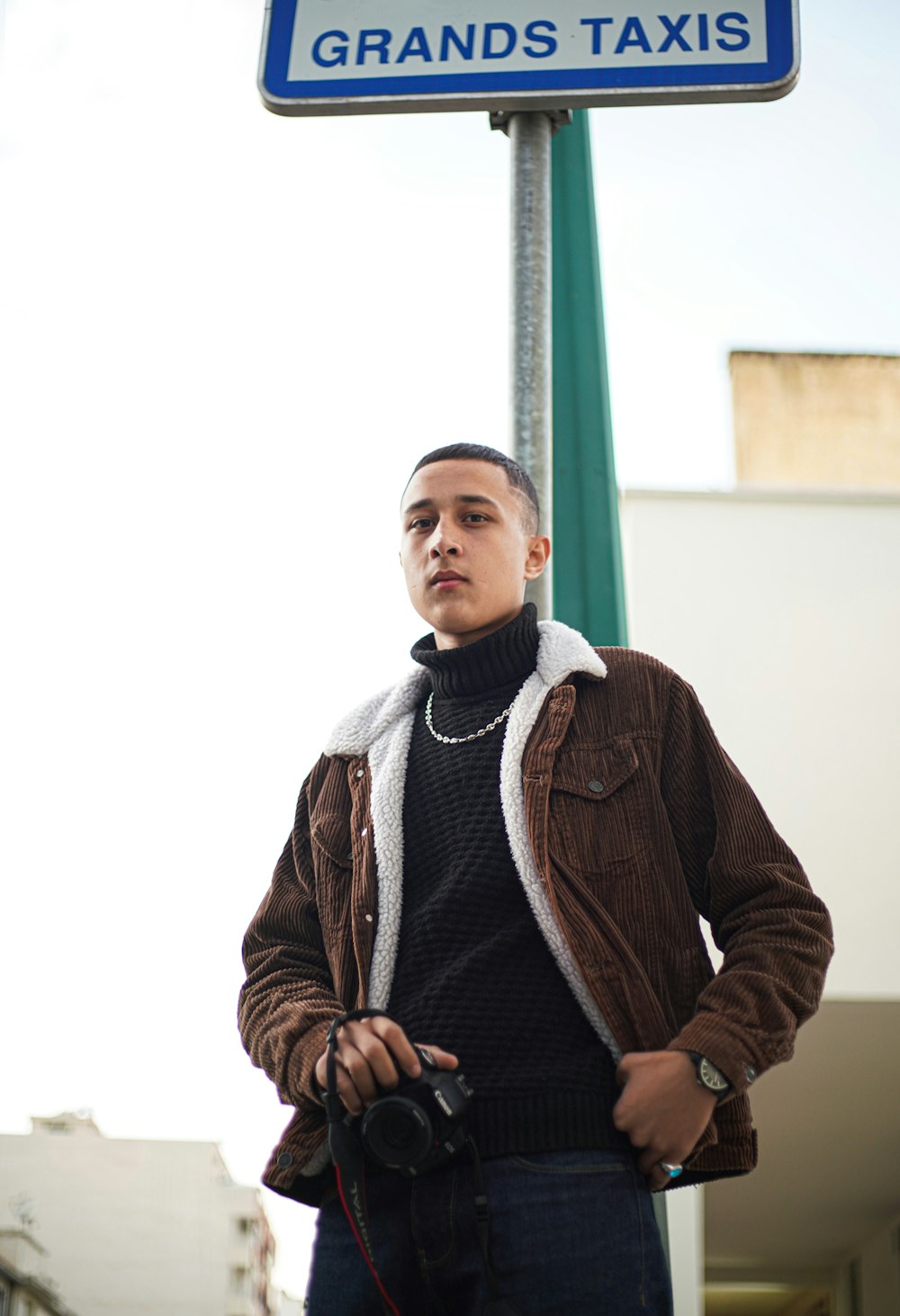 man in brown zip up jacket standing beside green metal pole