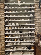Assortment of colorful tea cups and teapots arranged on a cozy wooden shelf.