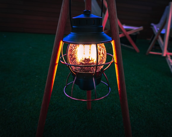 A classic outdoor side table holding a glowing lantern beside a cozy seating area.