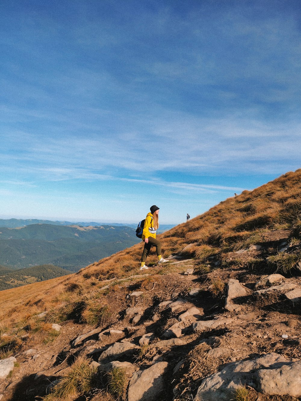 man in yellow shirt and black shorts standing on brown rock mountain during daytime