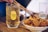 A chilled glass of Suntory Whisky filled with ice sits on a wooden table next to a bowl of crispy, thinly sliced lotus root chips. Chopsticks are picking up one of the chips, emphasizing a relaxed, casual dining atmosphere.