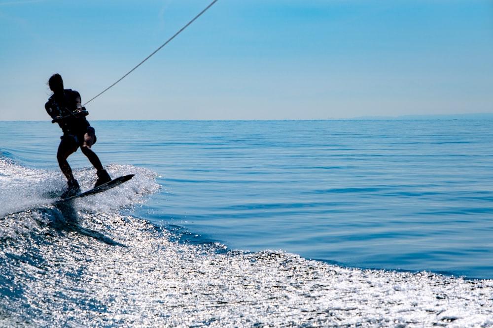 Mann im schwarzen Neoprenanzug Surfen auf blauem Meer unter blauem Himmel tagsüber