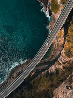 A winding coastal road in Europe viewed from above with a van driving along.