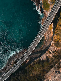 Cinematic shot of a van winding through a coastal highway with rugged cliffs and ocean waves below.