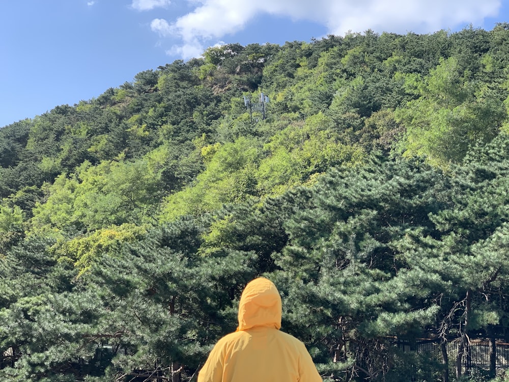 person in orange hoodie standing on brown dirt road in front of green trees during daytime