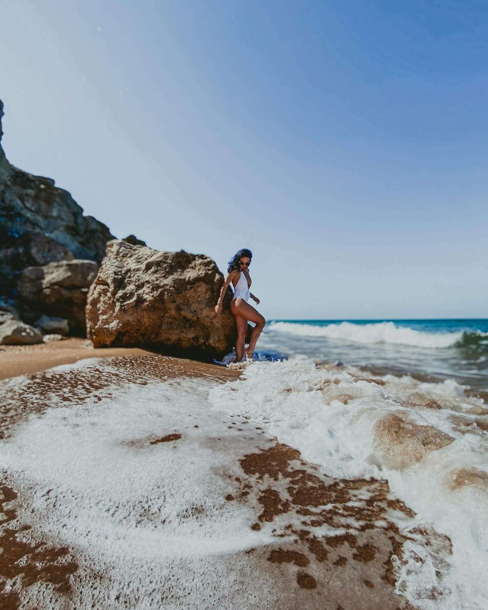 woman in black tank top and blue denim shorts standing on white sand beach during daytime