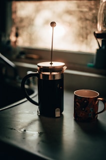 Elegant coffee grinder and French press set on a kitchen counter bathed in morning light.