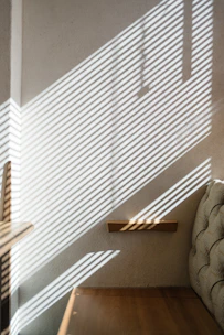 Sunlight filtering through sleek, modern blinds casting striped shadows on a minimalist living room wall.