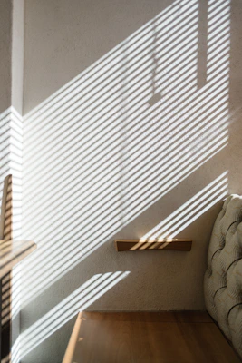 Sunlight filtering through sleek, modern blinds casting striped shadows on a minimalist living room wall.