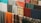 A collection of various colorful fabrics and textiles are hung in a row. The fabrics display a range of patterns, including plaid, floral, and solid designs. Materials appear to be made of different textures, such as wool or cotton, in an array of colors like orange, blue, green, and red.