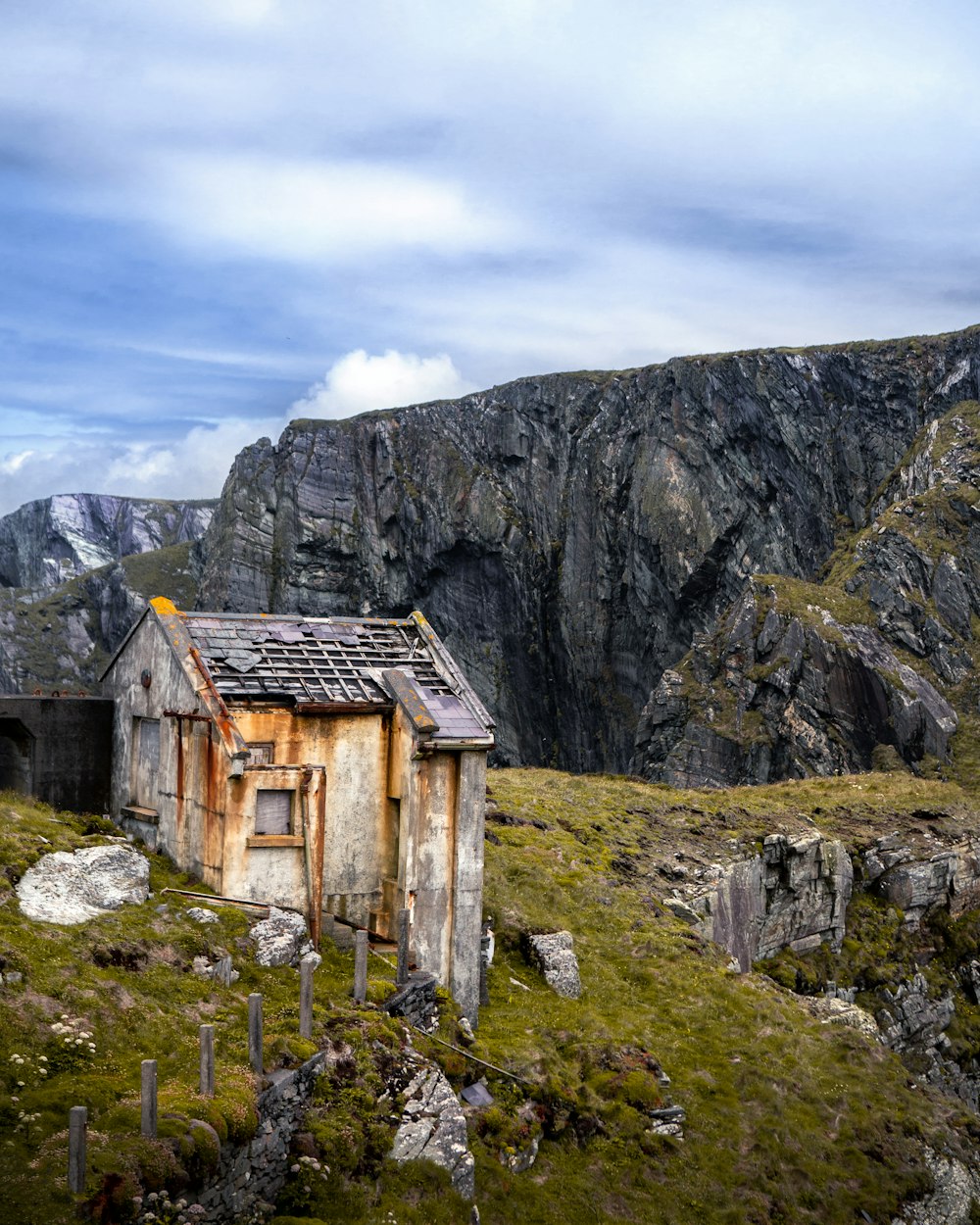 brown wooden house on green grass field near gray rocky mountain under white cloudy sky during