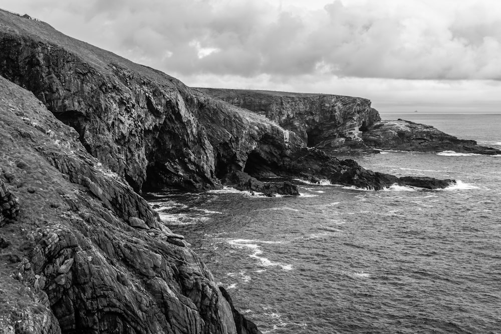 grayscale photo of rocky mountain beside sea