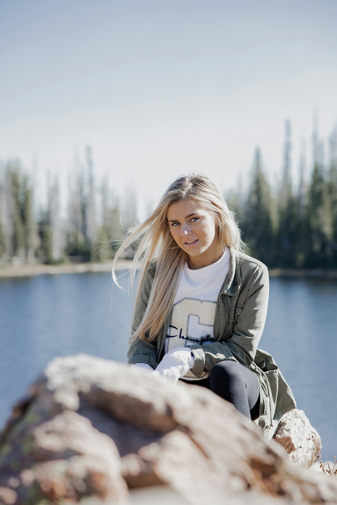 woman in gray jacket sitting on rock near body of water during daytime