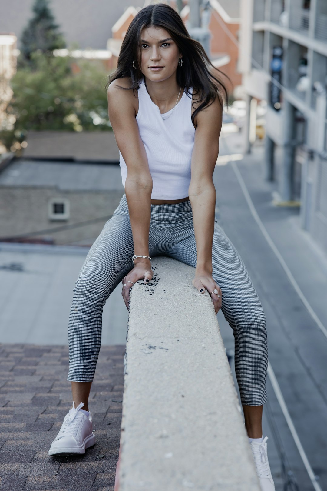 woman in white tank top and gray pants sitting on gray concrete road during daytime