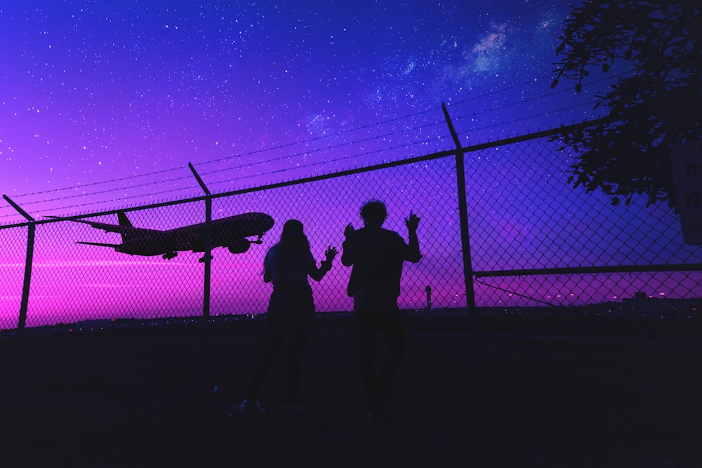 silhouette of 2 person standing beside fence during night time