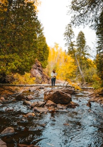 woman in white jacket standing on rock in river during daytime