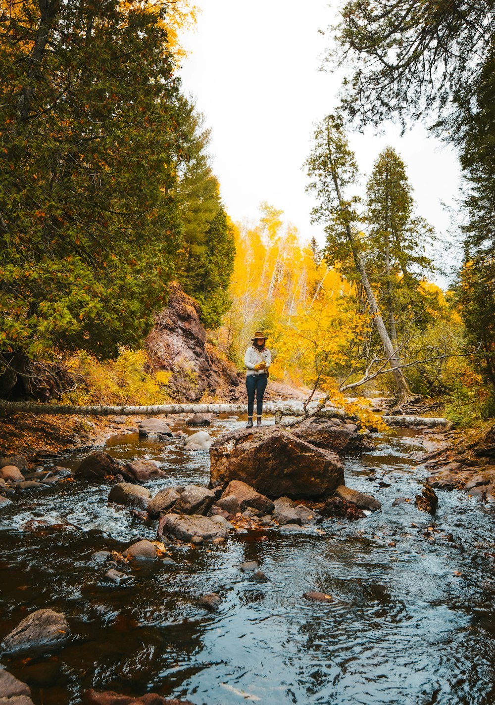 woman in white jacket standing on rock in river during daytime