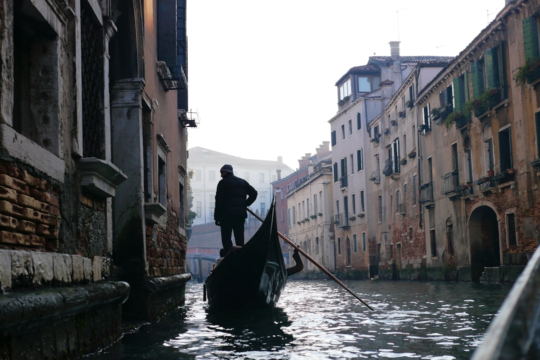 man in black jacket riding on boat on river between buildings during daytime
