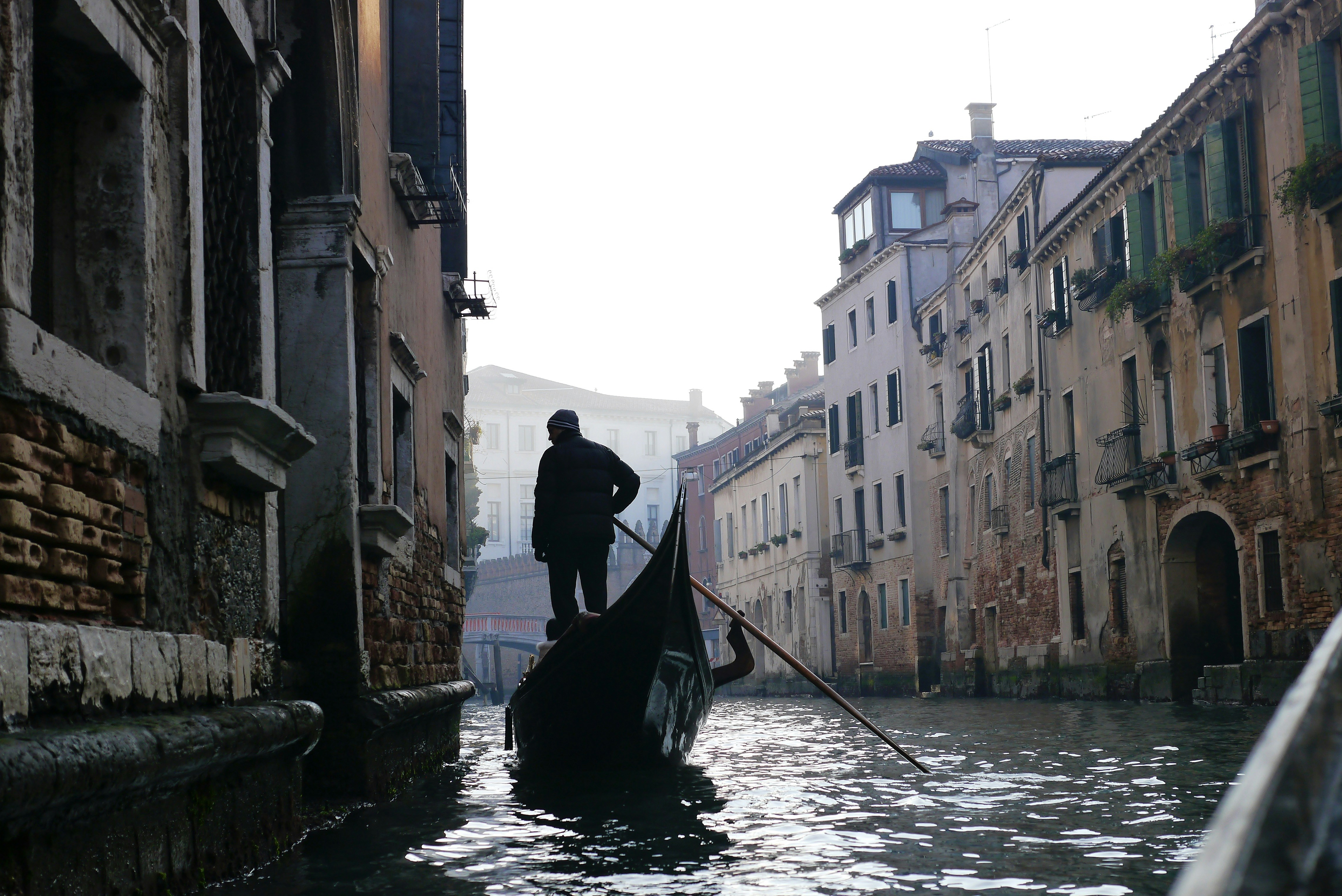 man in black jacket riding on boat on river between buildings during daytime
