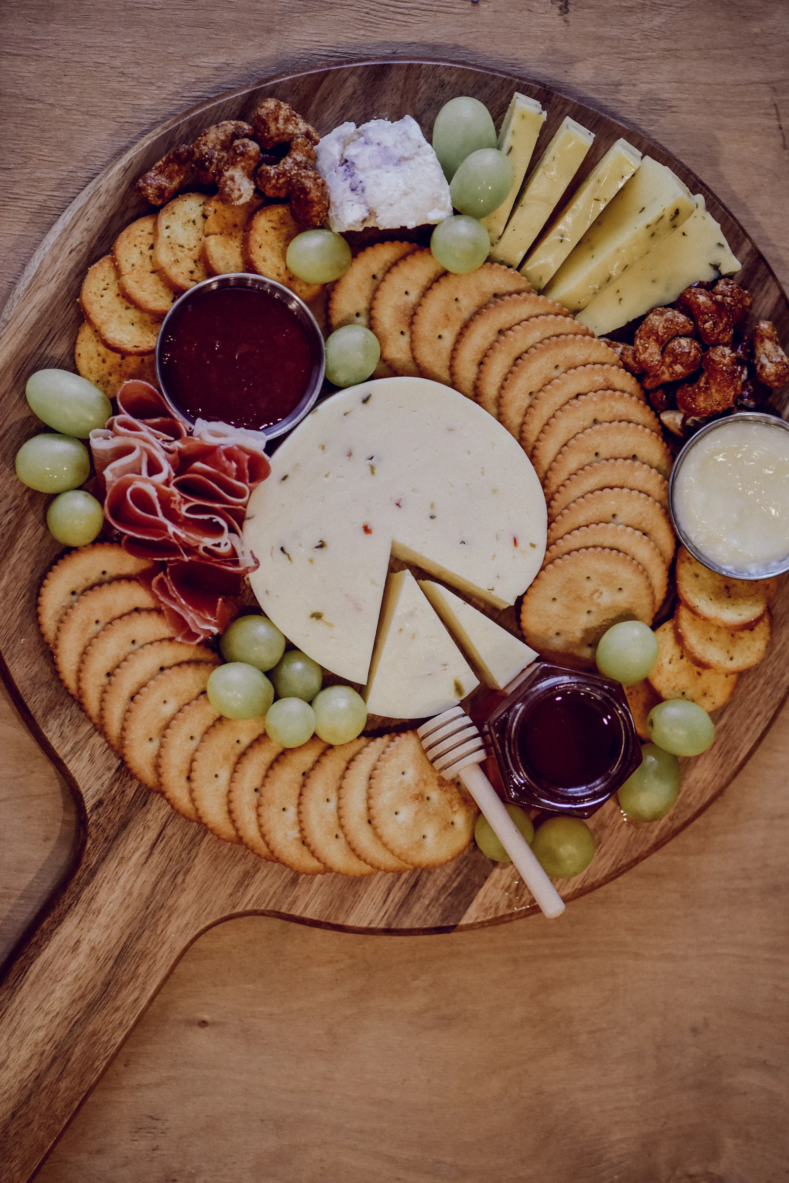 Planche en bois garnie de fromages, crackers, raisin, miel et fruits secs
