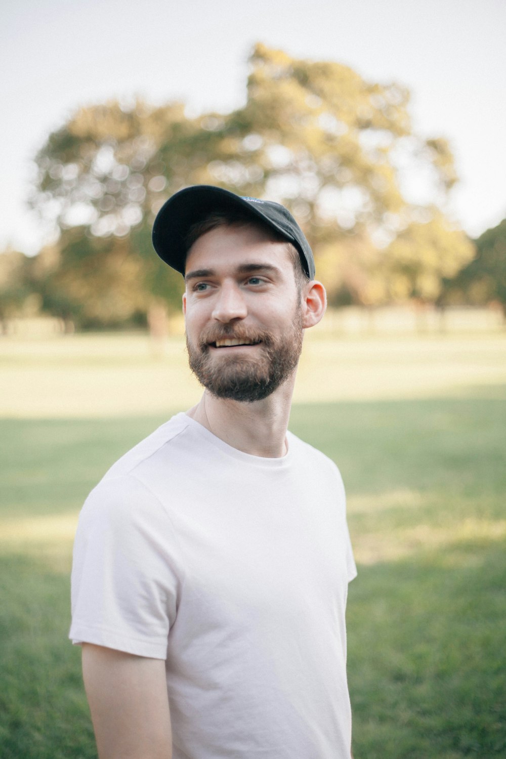 man in white crew neck shirt wearing black cap standing on green grass field during daytime