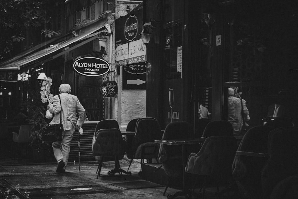 grayscale photo of man in jacket walking on sidewalk