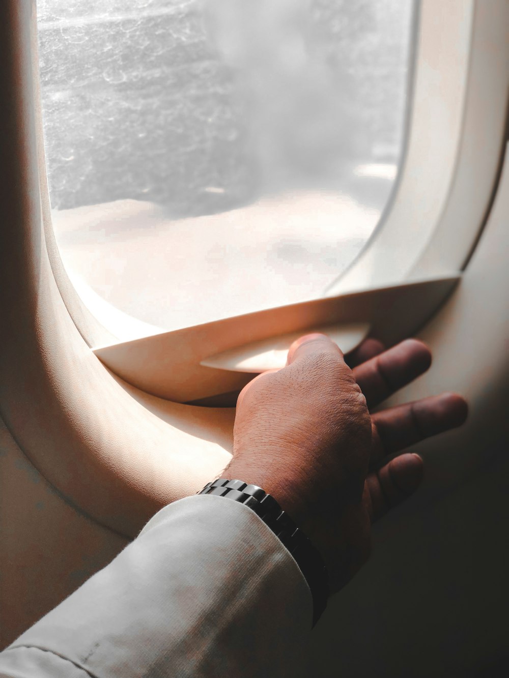 person wearing silver link bracelet watch holding airplane window