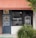 Front of a meal preparation business with a dark blue door and a large window displaying the name 'MEALPRO' and the slogan 'For the athlete in you.' The exterior features an orange awning and a small patch of greenery. A parked car is visible in the reflection of the window.