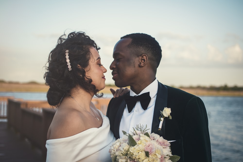 uomo in abito nero che bacia la donna in abito da sposa bianco