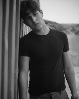 Young man wearing a black graphic t-shirt and cargo pants posing against an urban wall