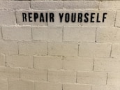 A concrete brick wall features the stencil-painted message 'REPAIR YOURSELF' in bold black letters.