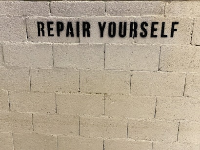 A concrete brick wall features the stencil-painted message 'REPAIR YOURSELF' in bold black letters.
