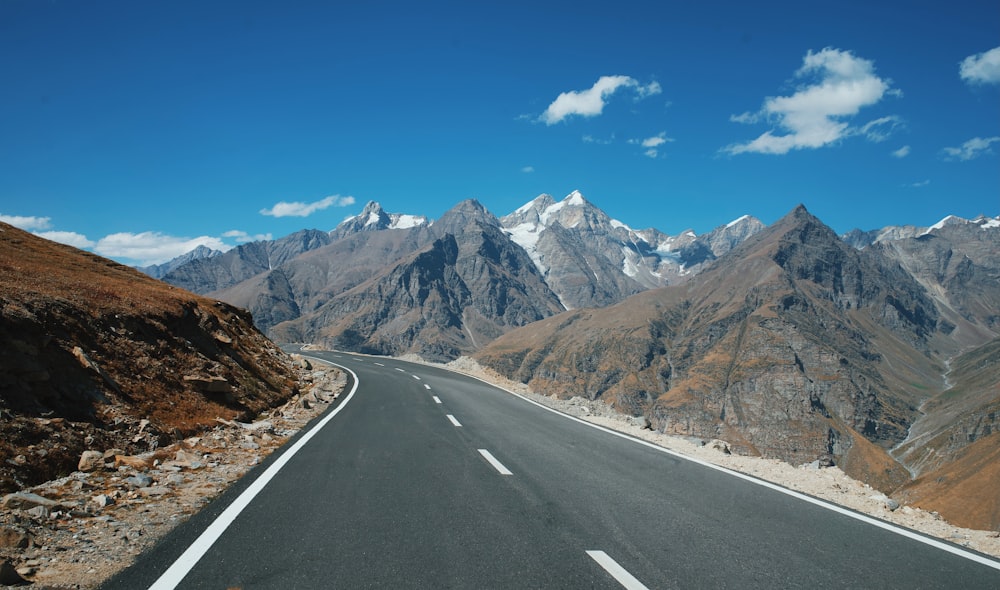 gray concrete road near brown rocky mountain under blue sky during daytime