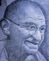 A close-up view of an intricately detailed engraving depicting an elderly man with glasses and a gentle smile. The image is rendered in a monochromatic color scheme, showcasing fine line work and texture.