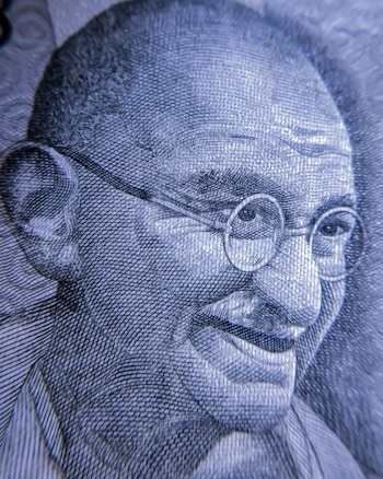 A close-up view of an intricately detailed engraving depicting an elderly man with glasses and a gentle smile. The image is rendered in a monochromatic color scheme, showcasing fine line work and texture.
