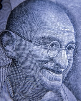A close-up view of an intricately detailed engraving depicting an elderly man with glasses and a gentle smile. The image is rendered in a monochromatic color scheme, showcasing fine line work and texture.