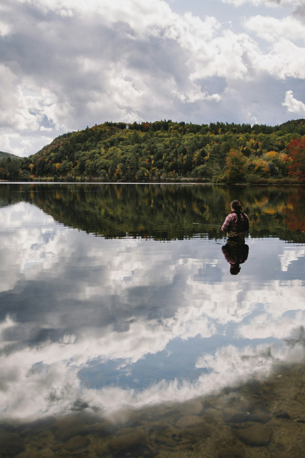 person in red jacket and black pants sitting on brown wooden dock during daytime