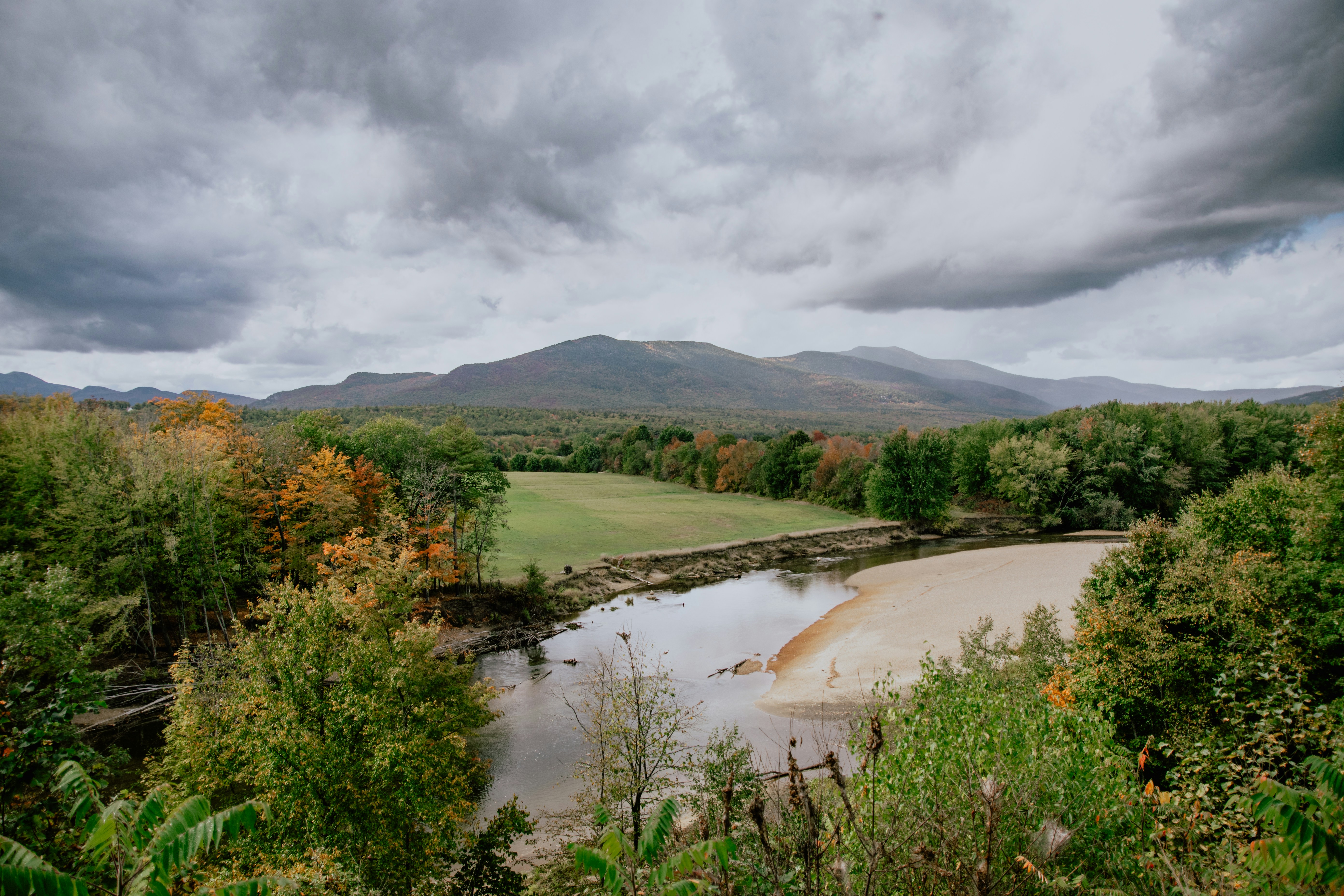 green grass field near lake under cloudy sky during daytime