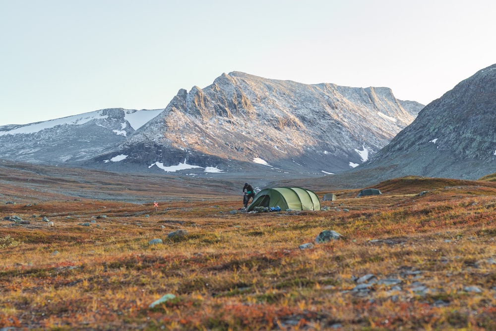 gray tent on green grass field near brown mountain during daytime